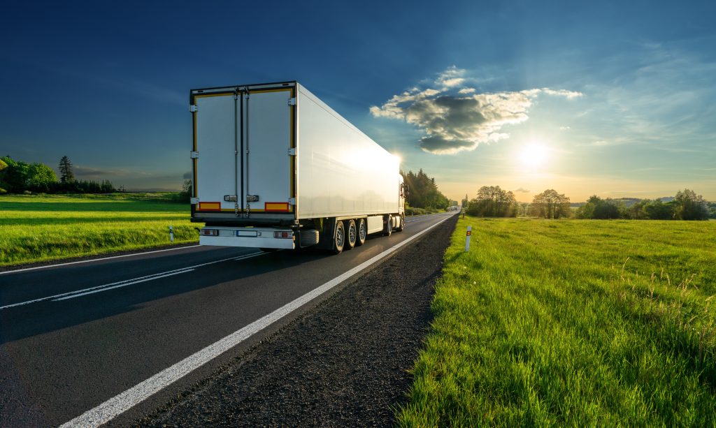 White truck driving on the asphalt road in a spring rural landscape at sunset