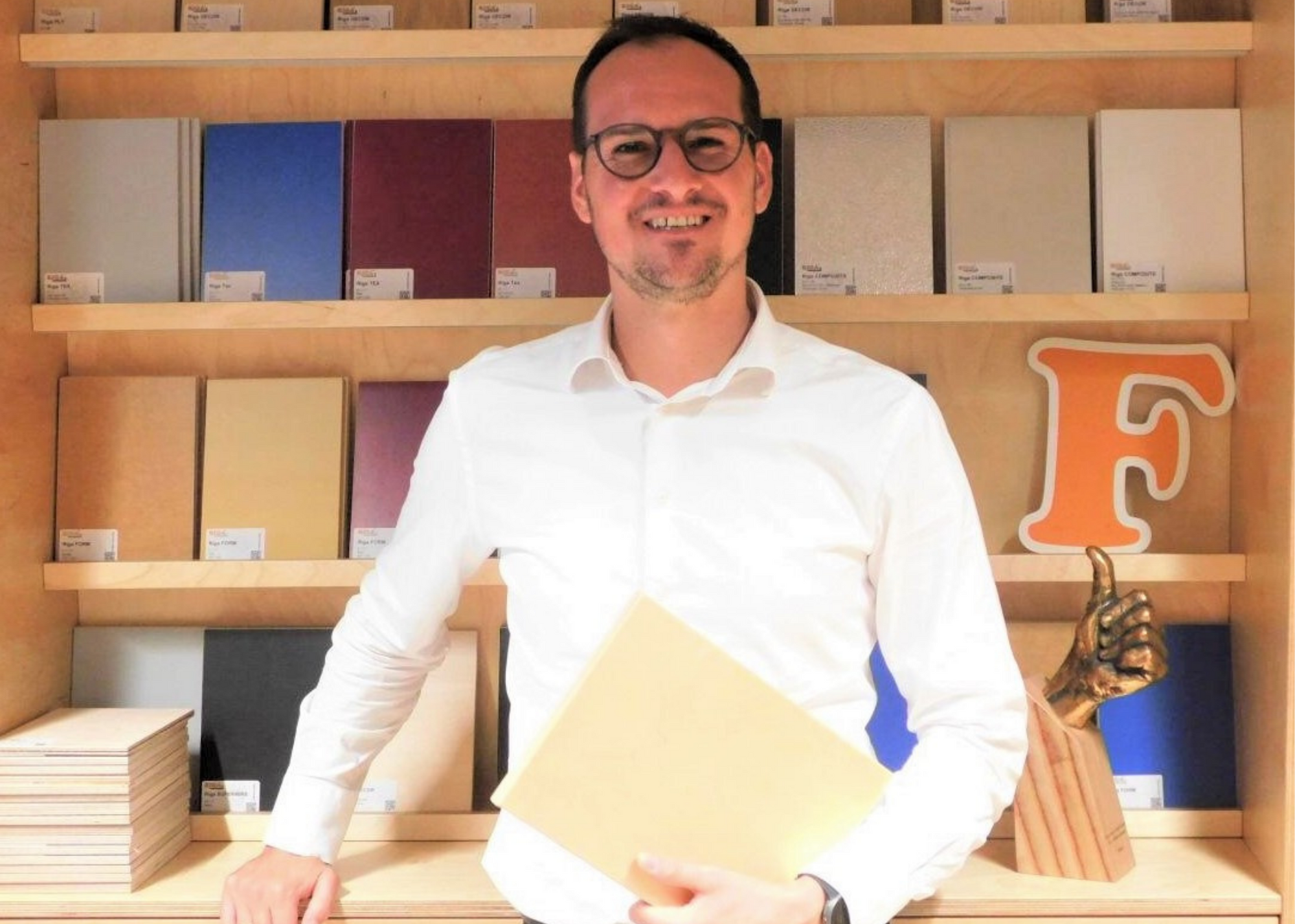 A man standing in front of a shelf with plywood samples in it while holding another plywood sample