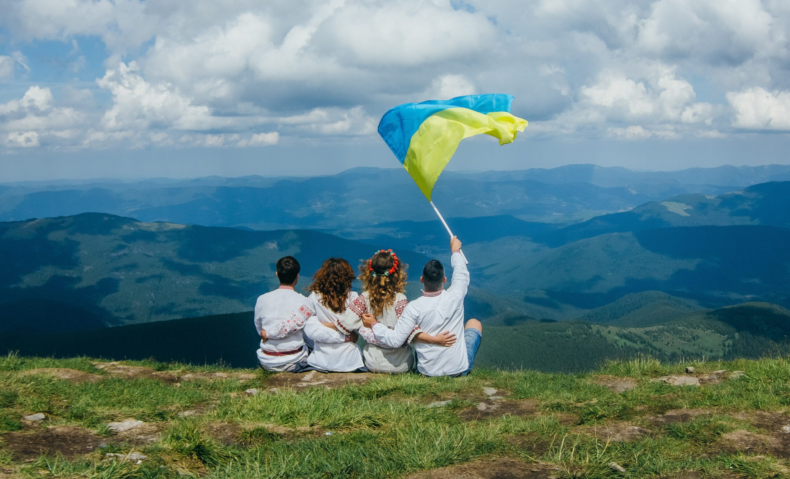 Četri draugi baltās drēbēs kalna virsotnē ar Ukrainas karogu