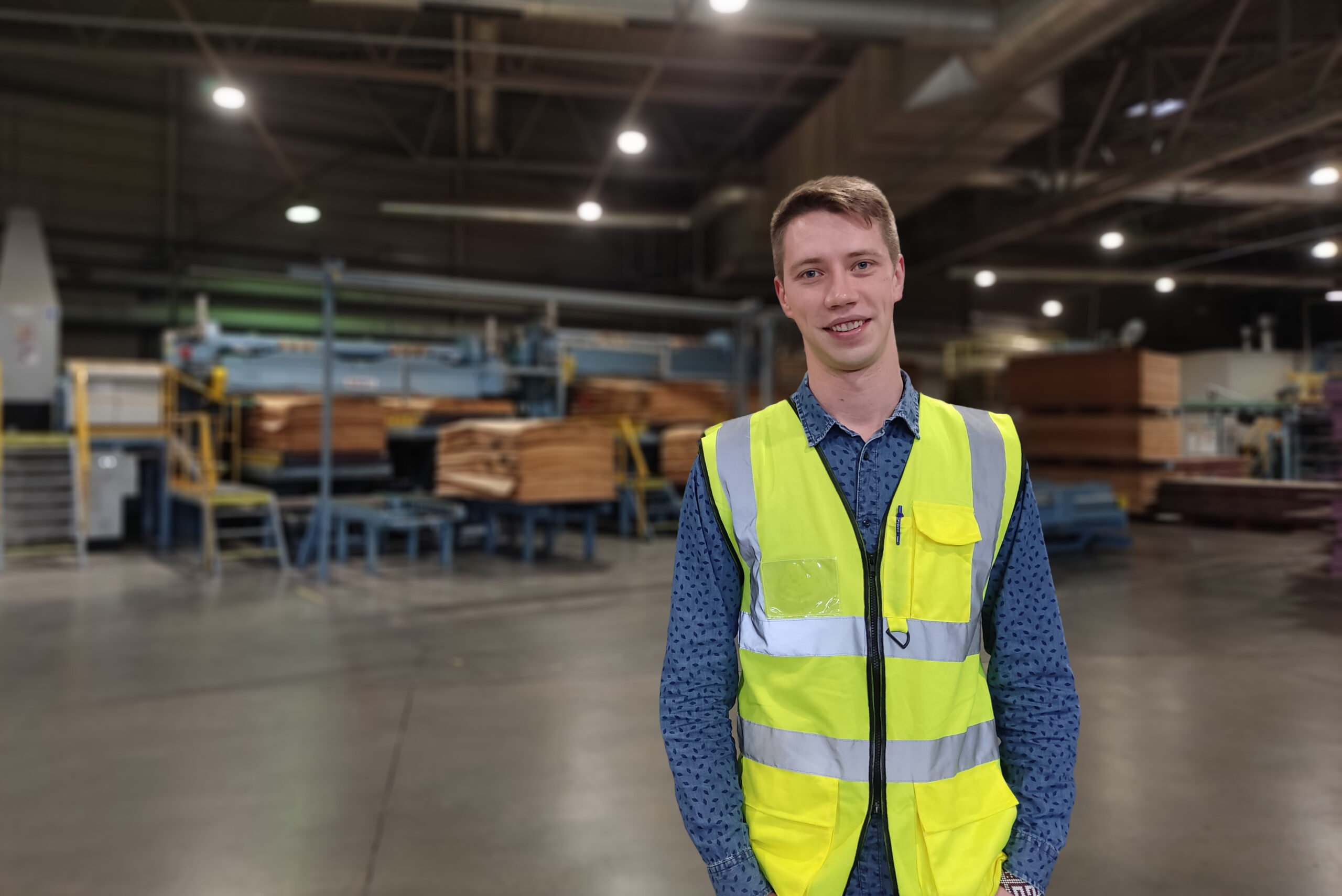 A man standing in a warehouse smiling in a reflective vest