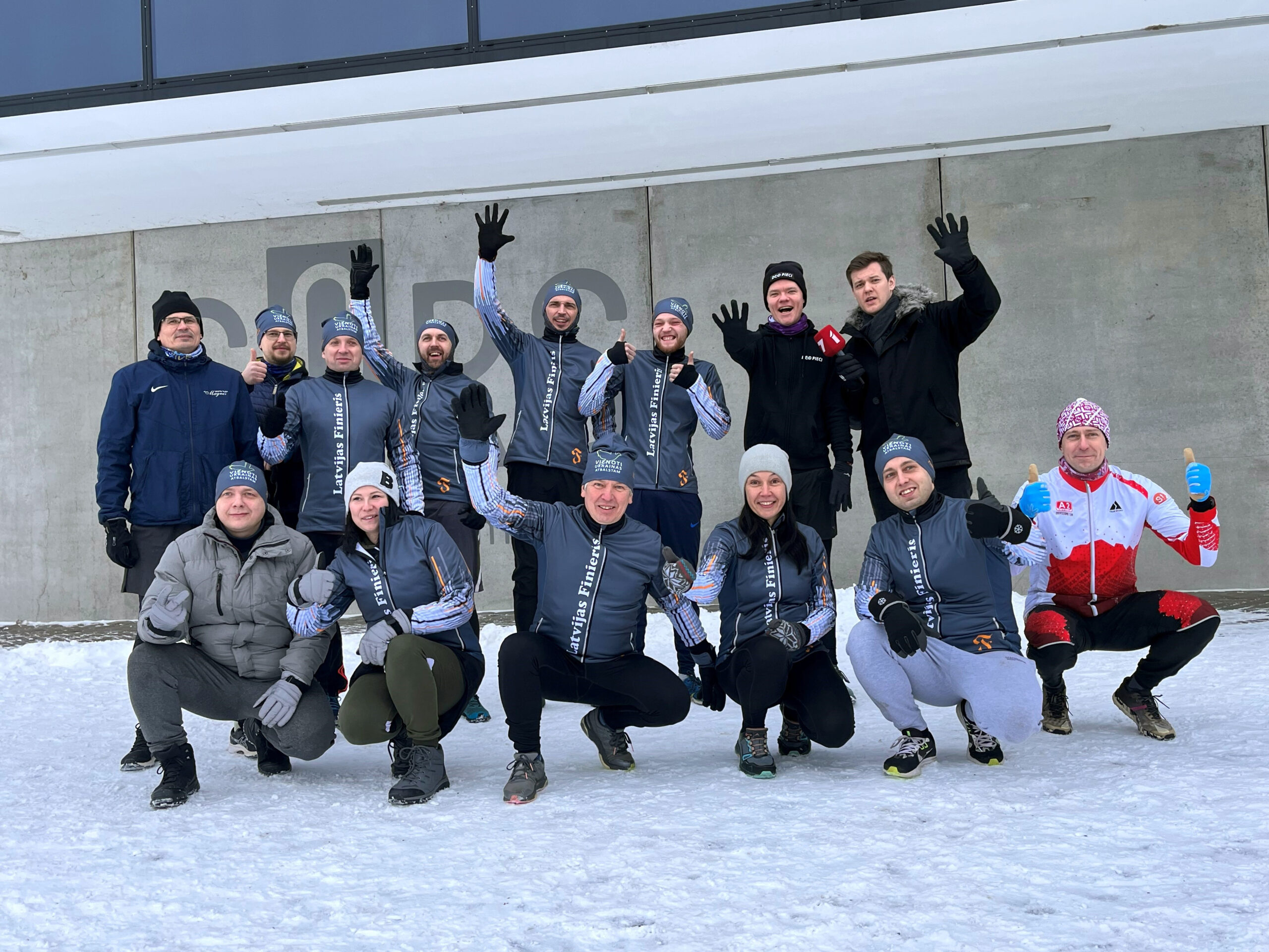 Grupa ar cilvēkiem sporta apģērbā smaida sniegā