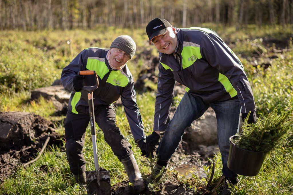 Two men holding a newly planted tree sapling