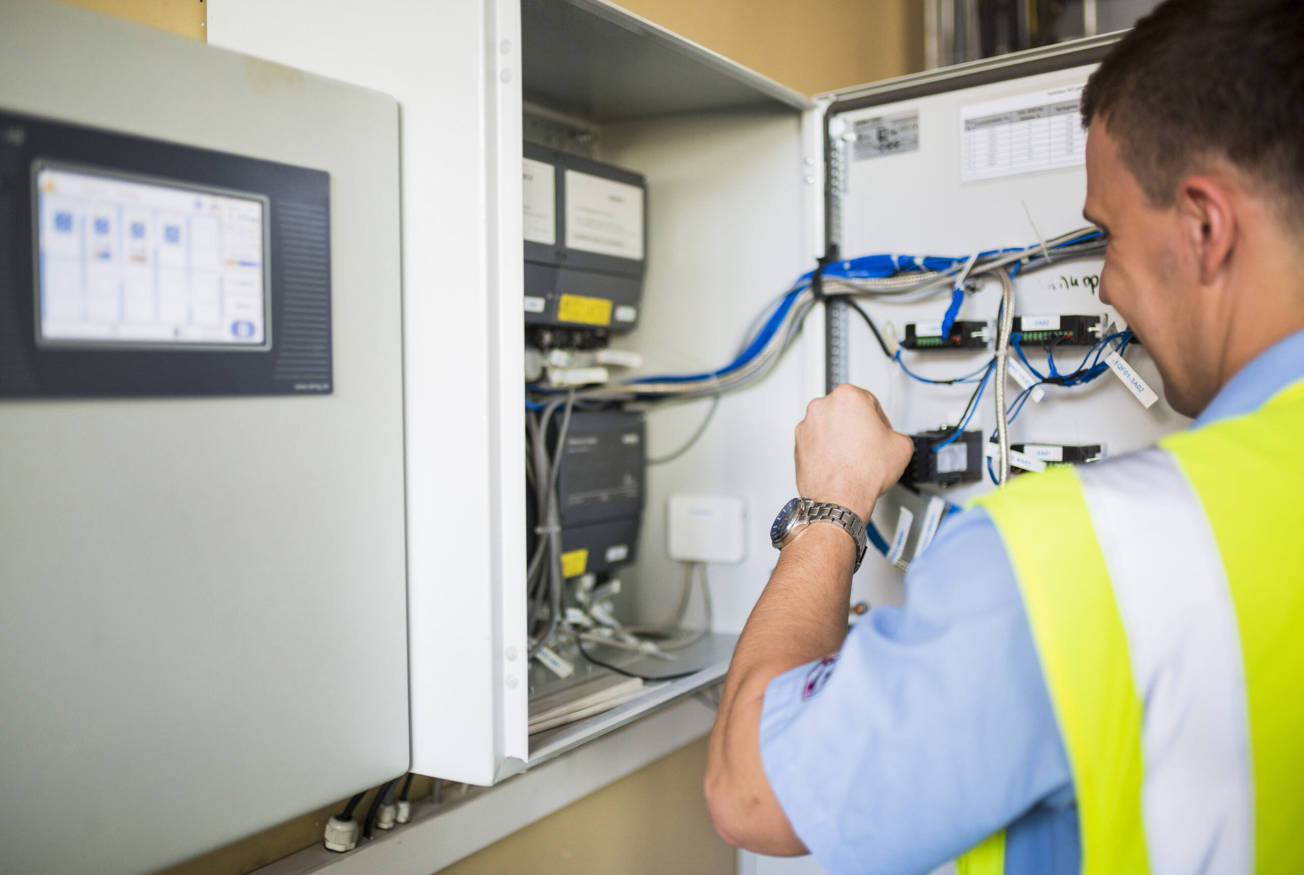Elektriķis atstarojošajā vestē strādā pie elektriskā skapja