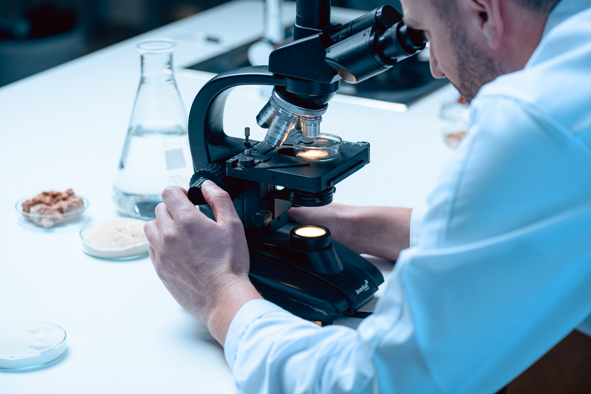 A scientist in protective gear in a laboratory looking at a sample through a microscope