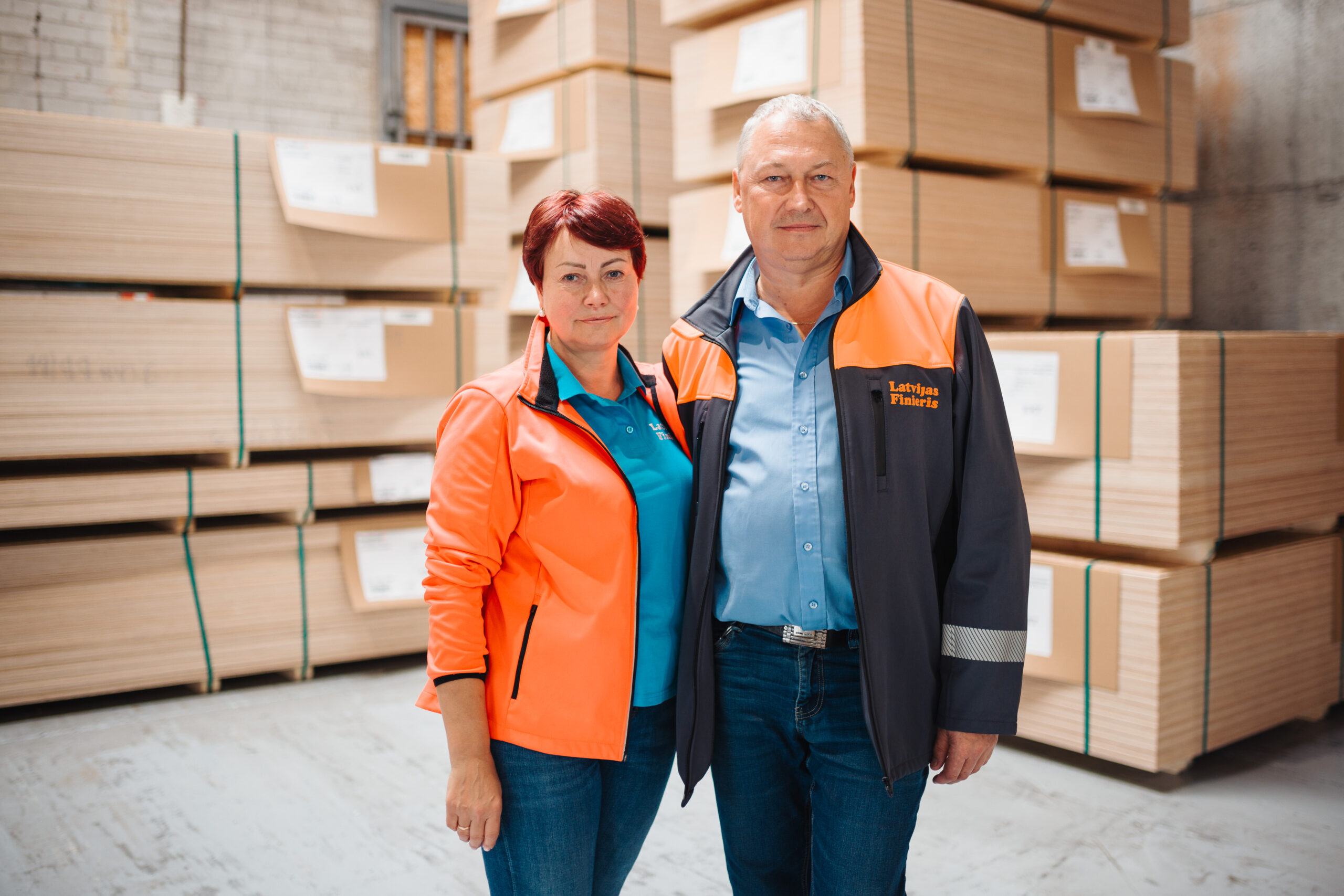 A man and a woman standing in a warehouse wearing "Latvijas Finieris" working merch